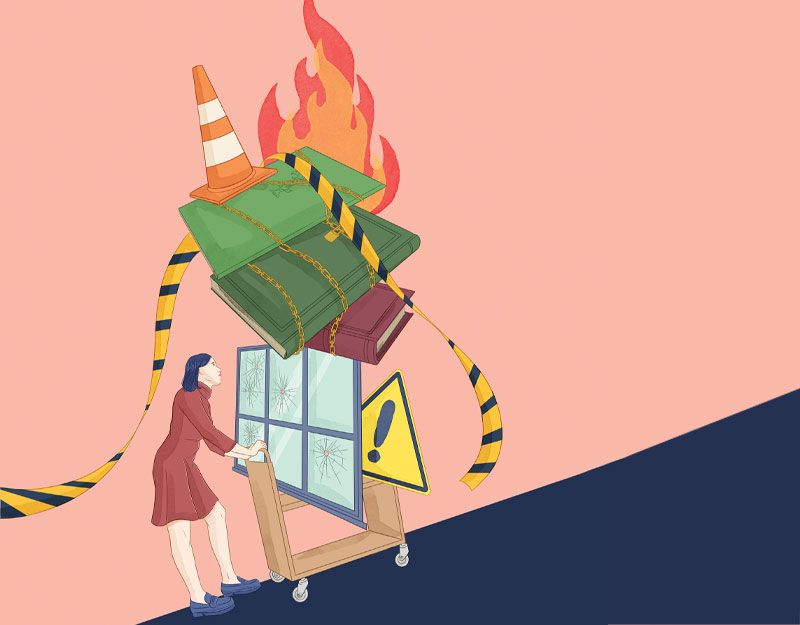 Women with library cart pushing up hill, filled with banned books on fire hazard sign, road cone, and broken window; Illustration by Stephanie Singleton