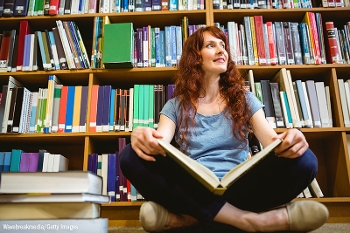 Woman reading a book, sitting on floor, in front of stacks