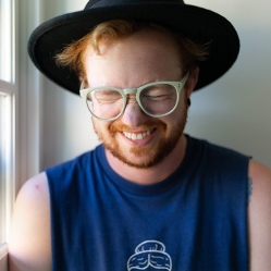 Redhead in a black hat and sleeveless dark shirt smiling
